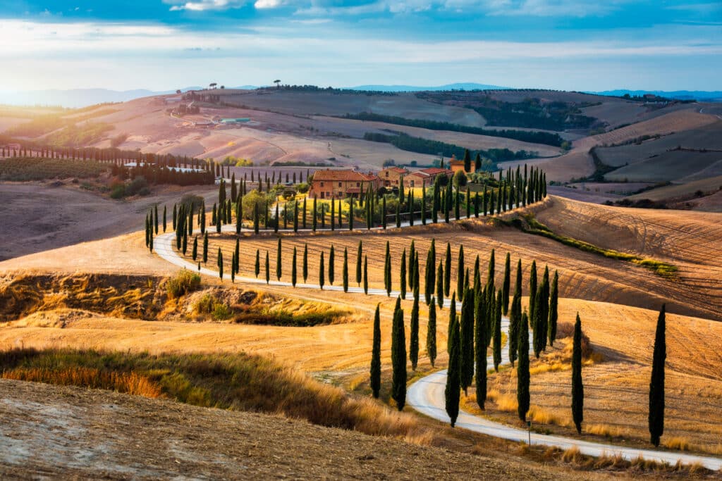 Paisagem toscana bem conhecida com campos de graos, ciprestes e casas nas colinas ao por do sol