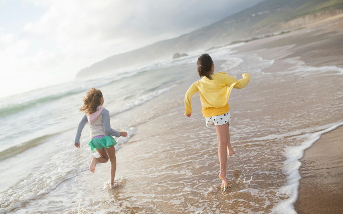 Crianças brincando na beira do mar em praia tranquila do Brasil, ideal para famílias com águas calmas e areia segura